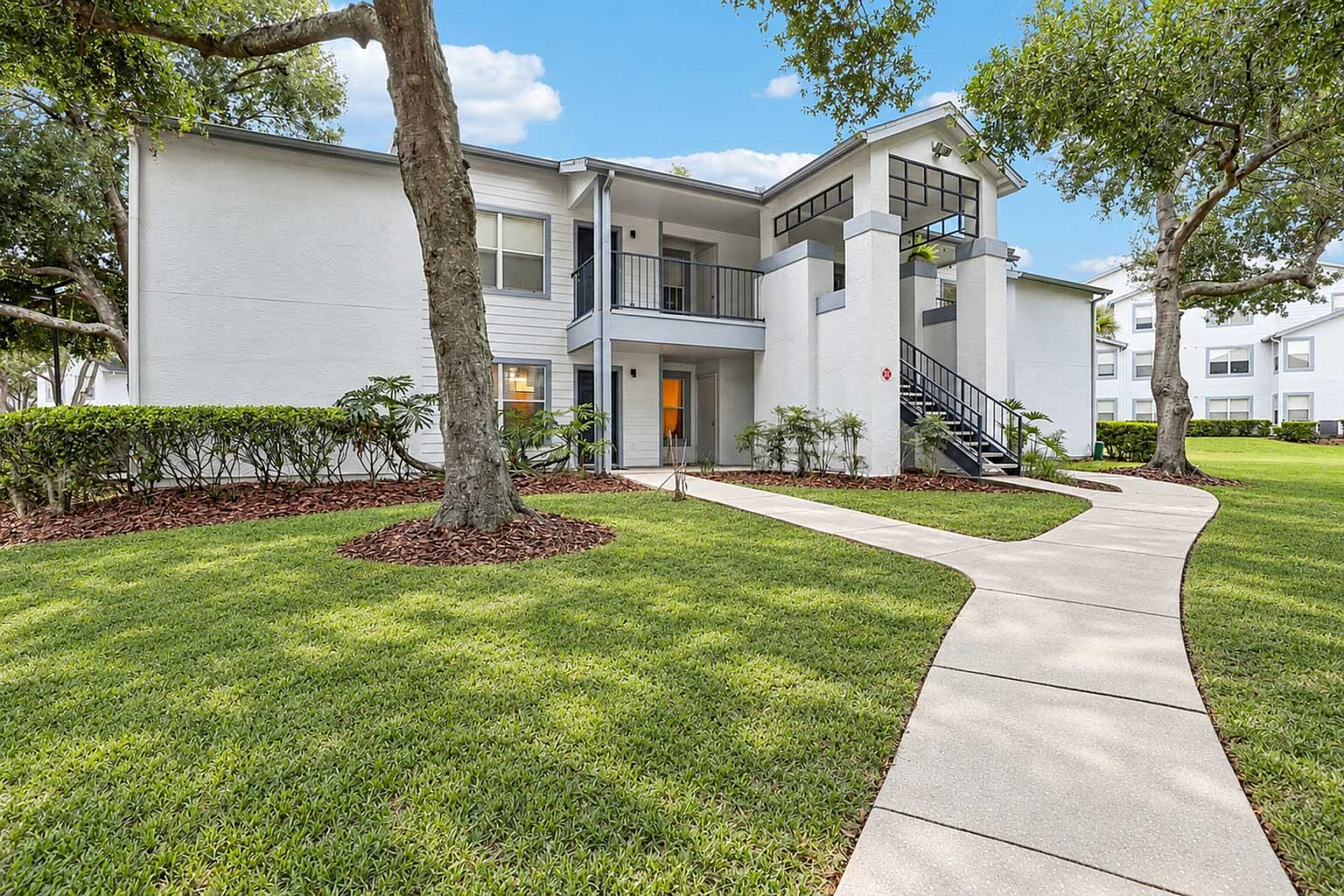 Charming white apartment building with lush green lawns and a curving walkway, offering serene living in a beautifully landscaped setting.