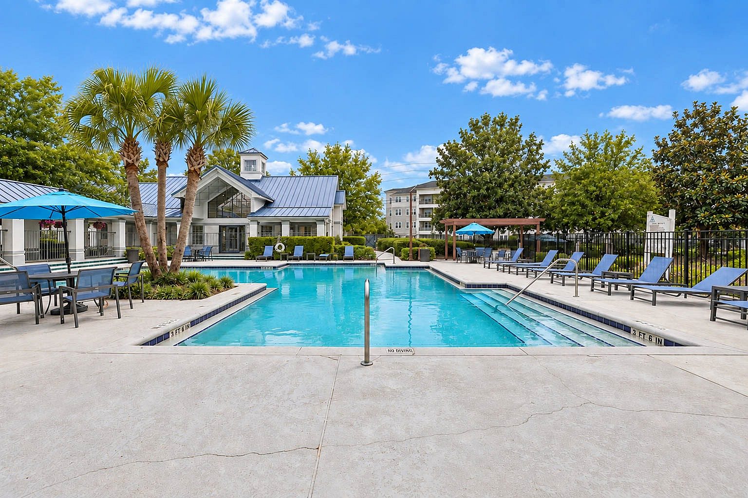 Inviting outdoor swimming pool area with lounge chairs, blue umbrellas, and lush greenery, perfect for relaxation and social gatherings.