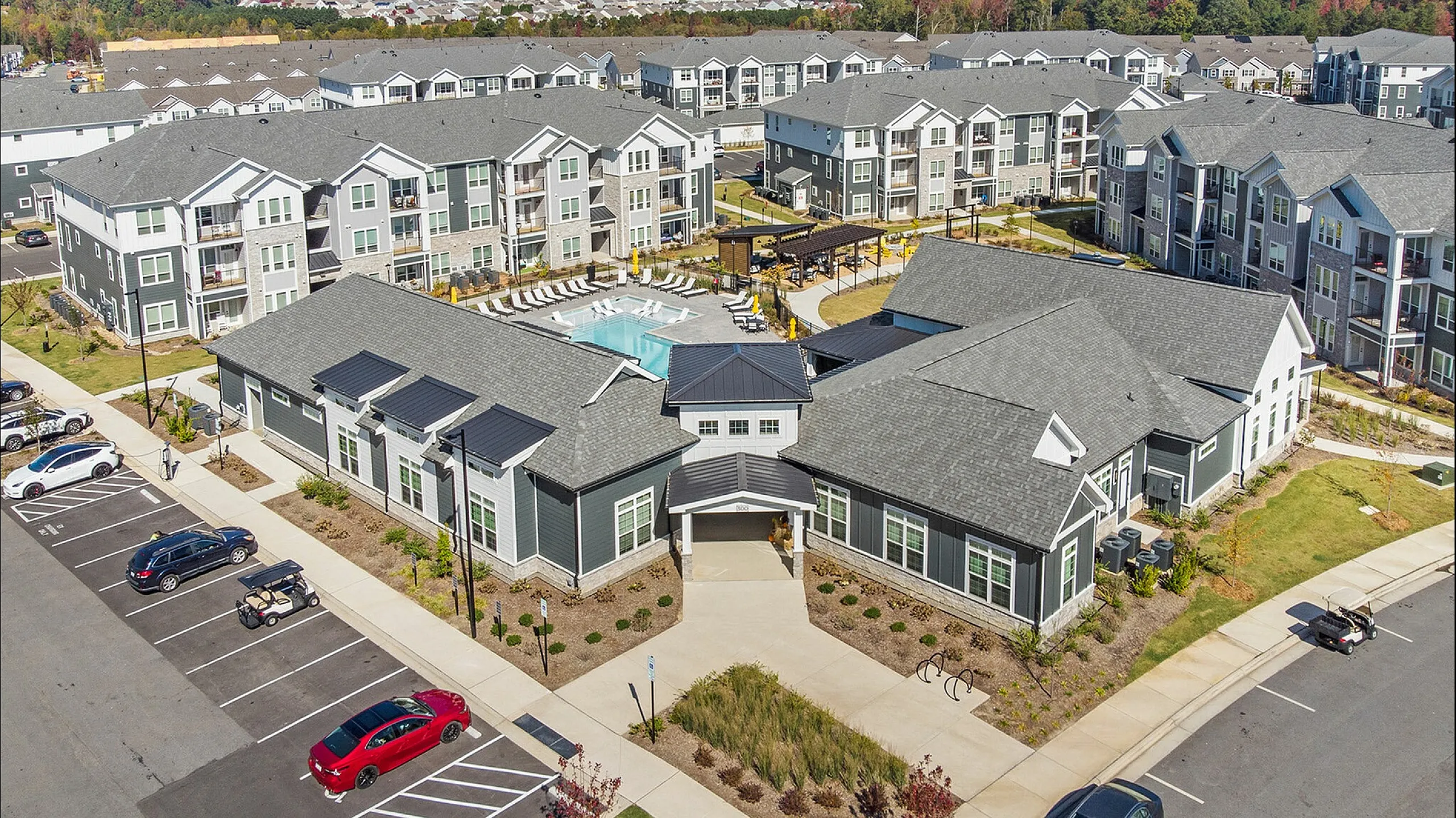 Aerial view of a modern apartment complex with a central swimming pool and surrounding greenery.