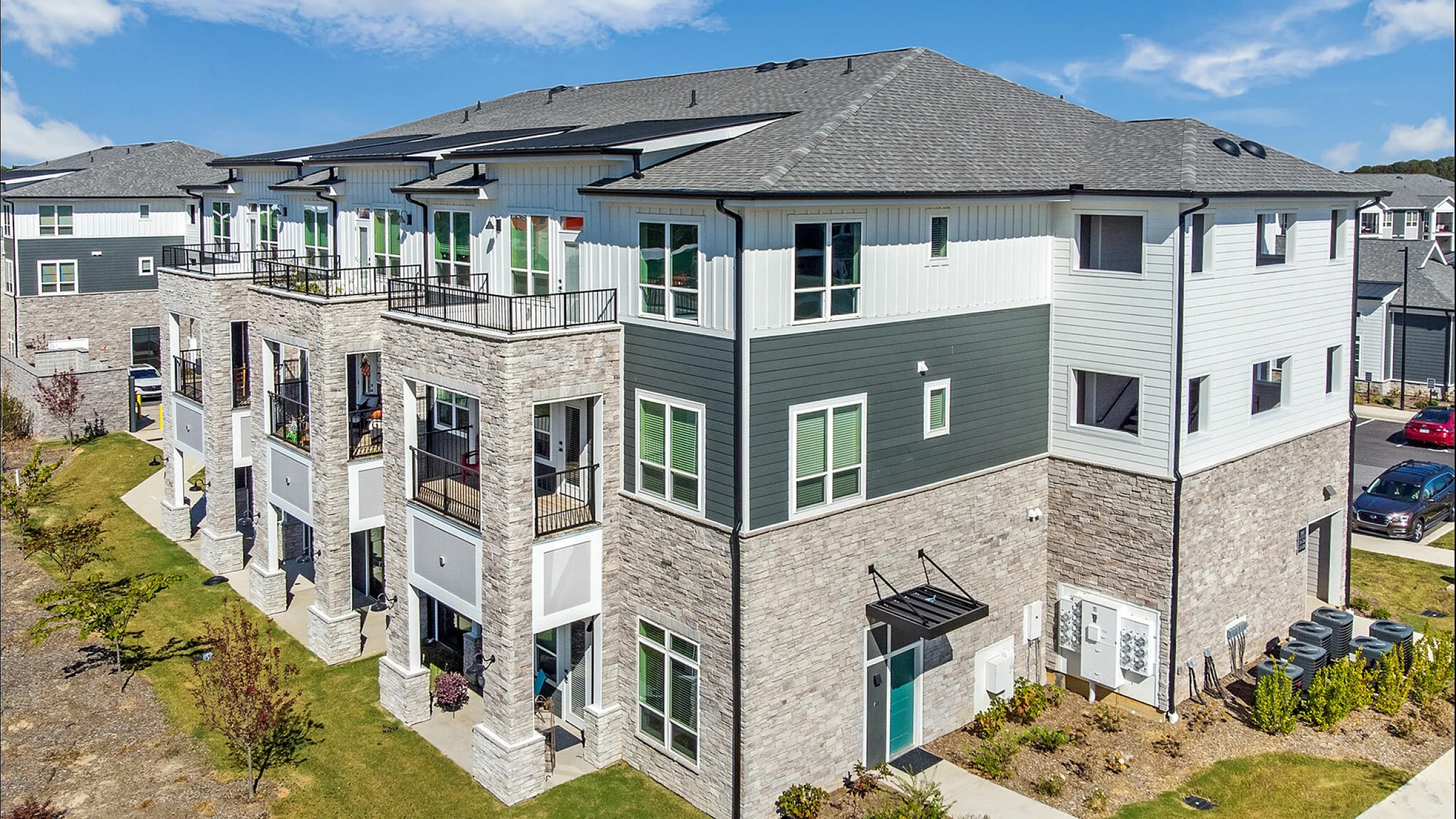 Contemporary three-story apartment building with balconies and manicured surroundings under a clear blue sky.