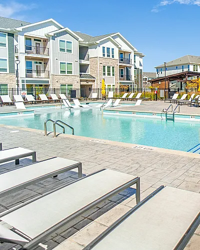 Modern apartment complex with a large outdoor swimming pool and sun loungers.
