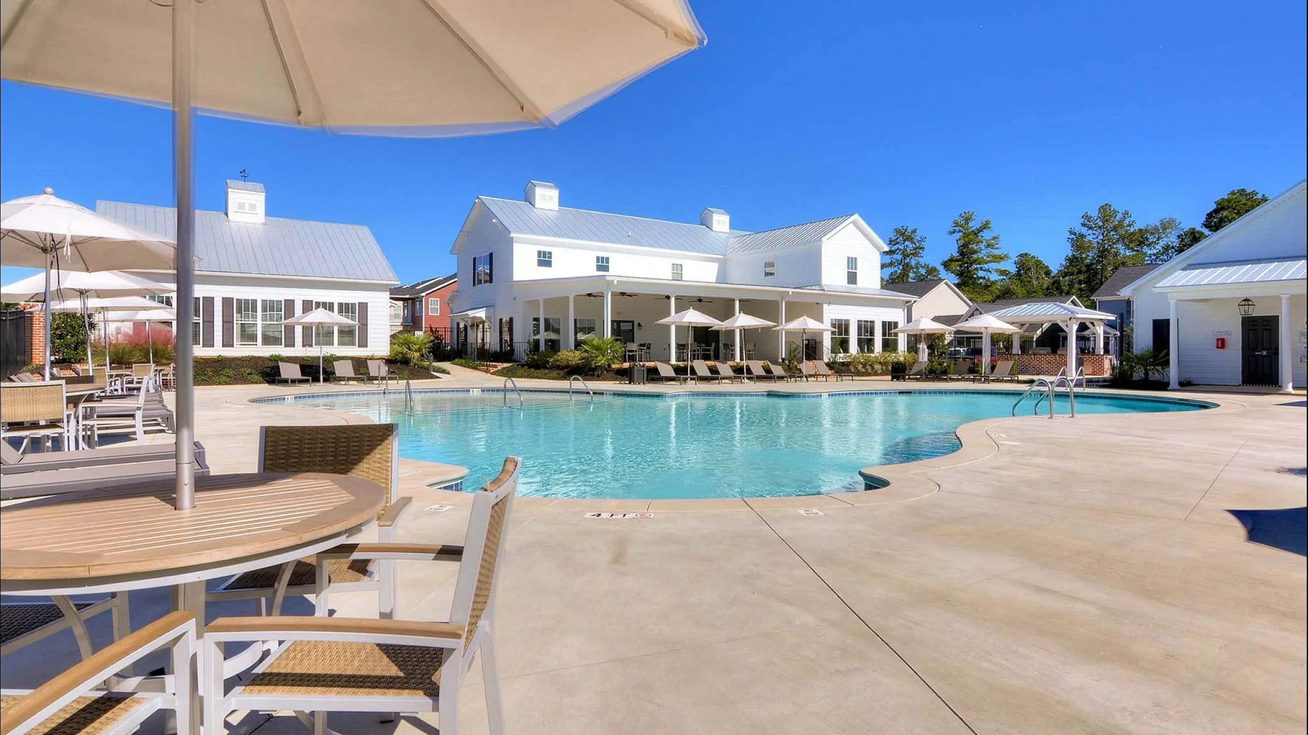 Gorgeous apartment complex with a sparkling swimming pool and elegant white buildings under a clear blue sky.