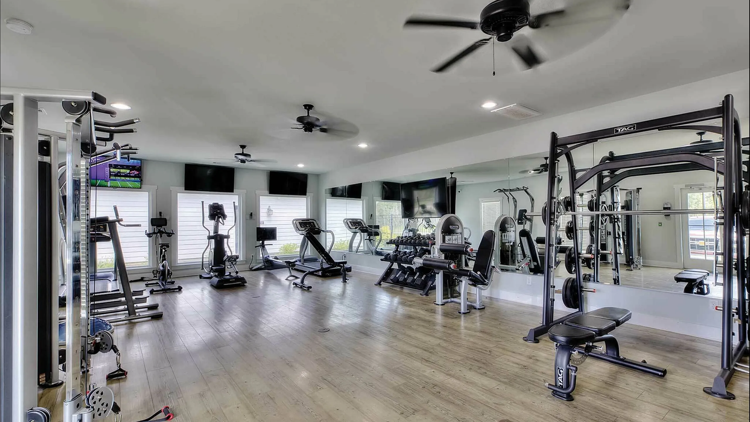 Spacious modern gym with various fitness equipment, large mirrors, and wood flooring.