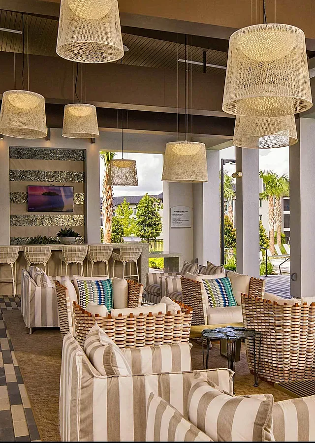 Modern outdoor lounge area with striped seating and hanging lights near a pool surrounded by blue umbrellas and greenery.