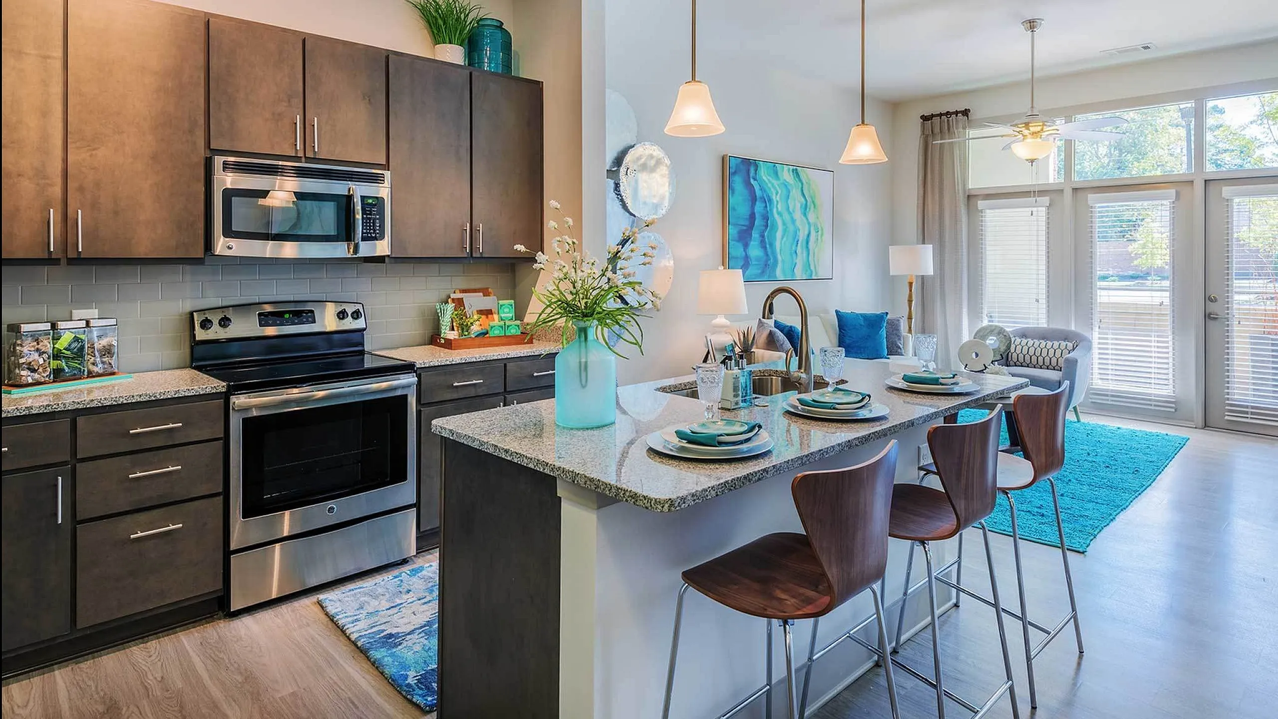 Elegant kitchen and living area with stylish decor, featuring stainless steel appliances, granite countertops, and large windows overlooking a scenic view.