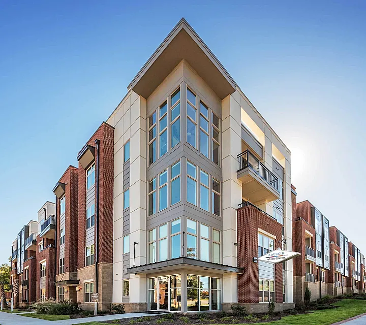 Contemporary apartment building with large windows and balconies in a sunny setting.