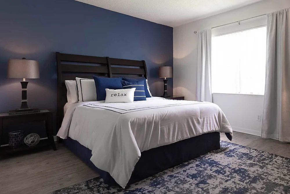 Stylish bedroom with blue accent wall, elegant bedding, and natural light.
