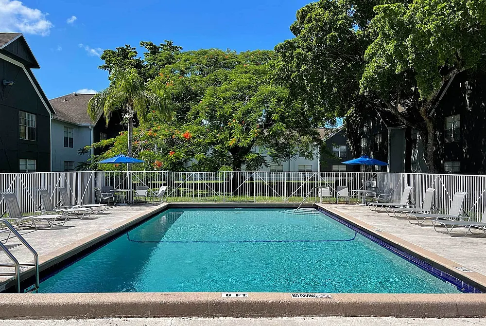 Sparkling apartment pool surrounded by lush greenery and sun loungers.