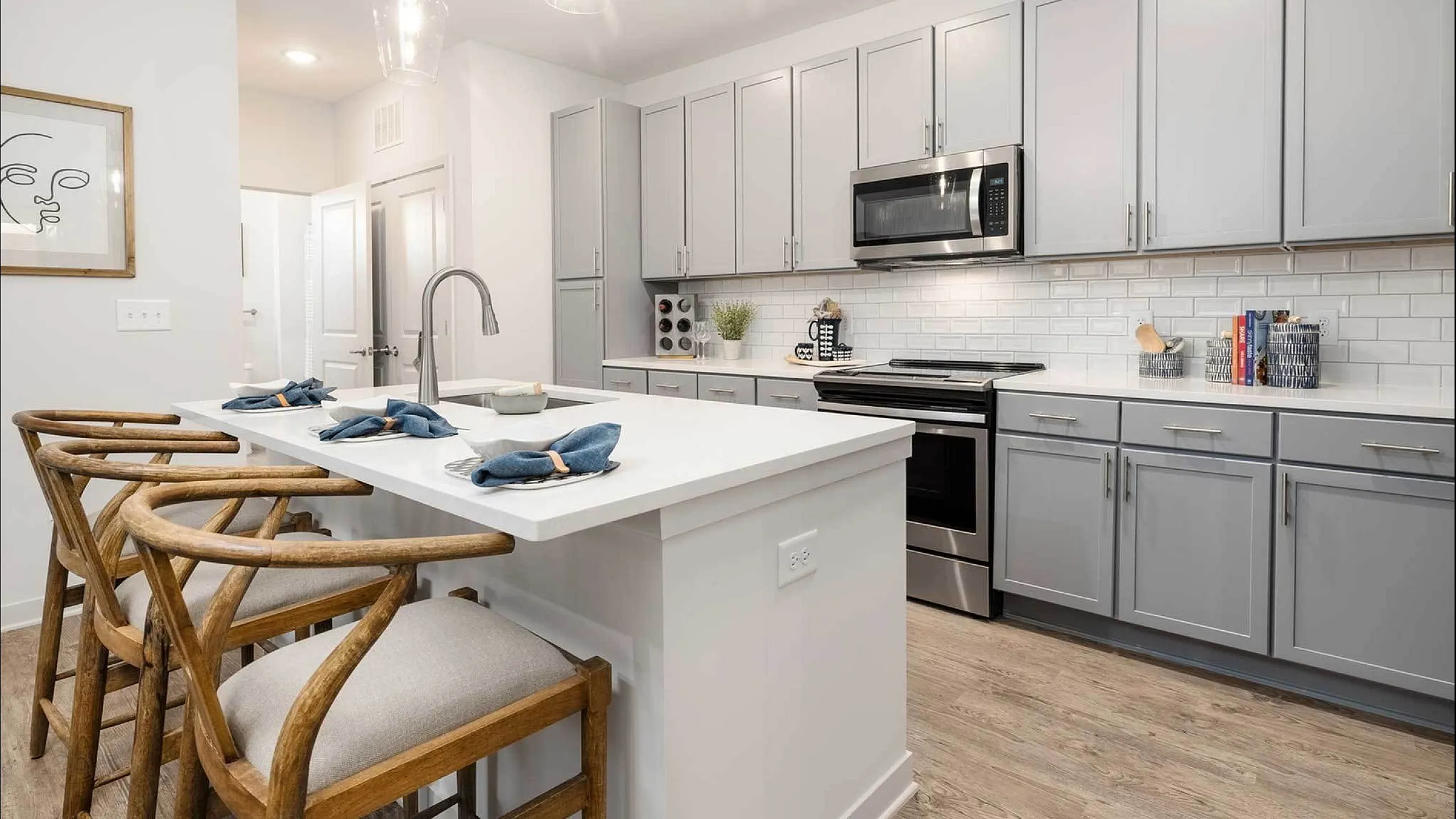 Contemporary kitchen with sleek appliances and wooden bar stools under pendant lights.