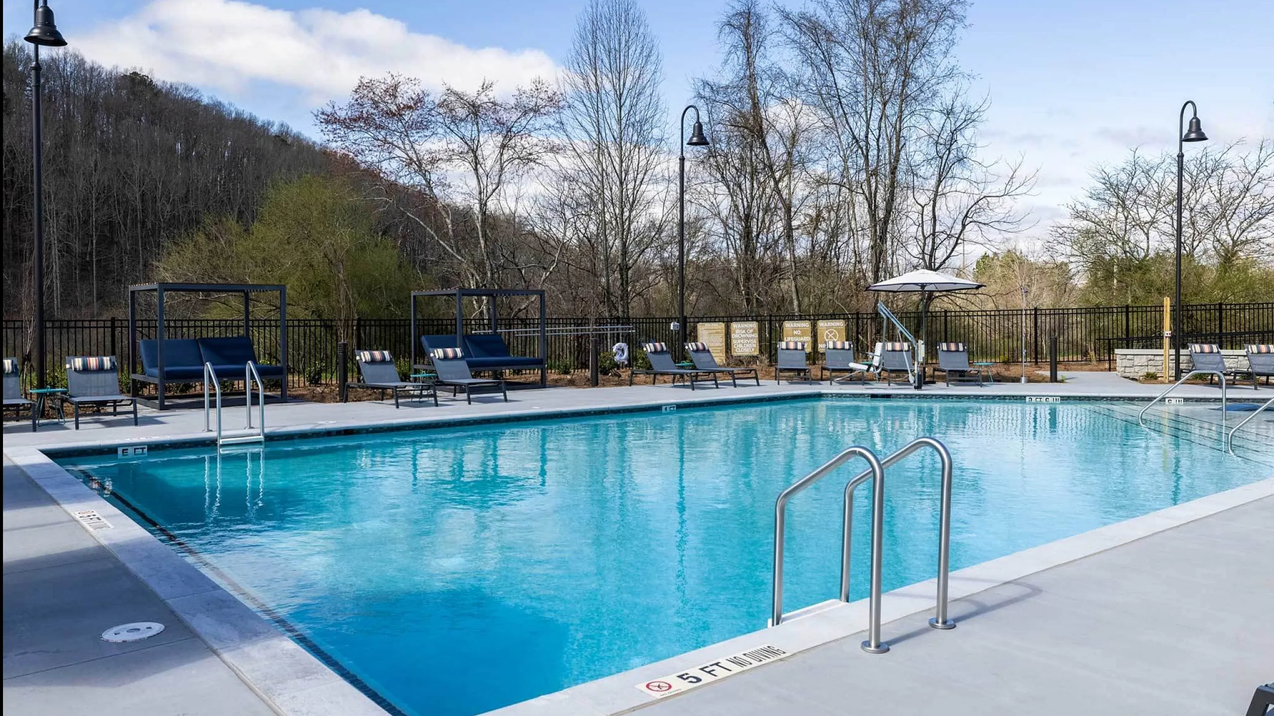 Tranquil outdoor swimming pool with lounge chairs and scenic view of trees