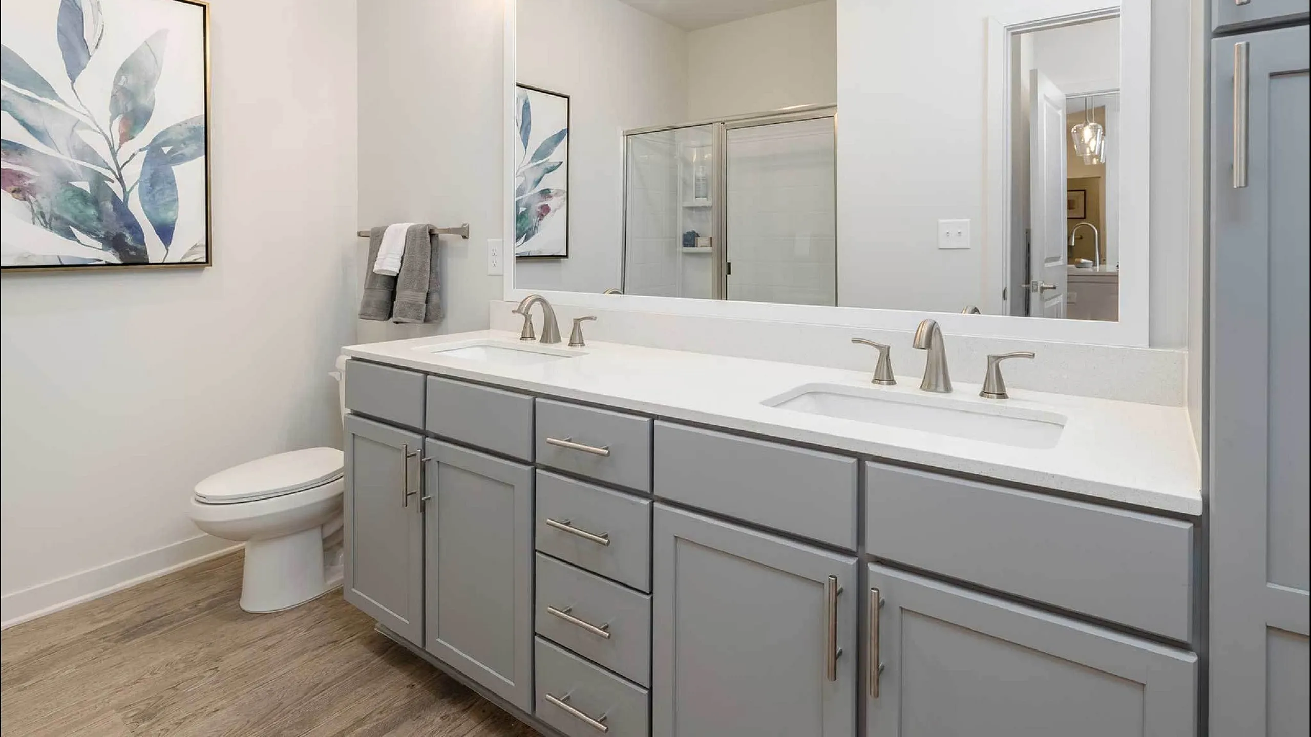 Modern bathroom with dual sinks, elegant grey cabinetry, large mirror, and stylish artwork.