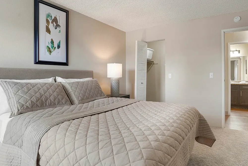 Spacious bedroom with a cozy bed and elegant decor, featuring a stylish lampshade and an open closet.