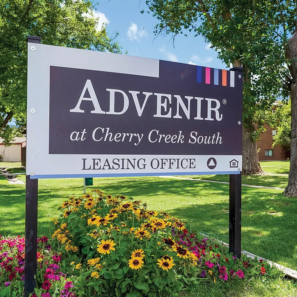 Leasing office sign at Advenir at Cherry Creek South surrounded by lush greenery and vibrant flowers.