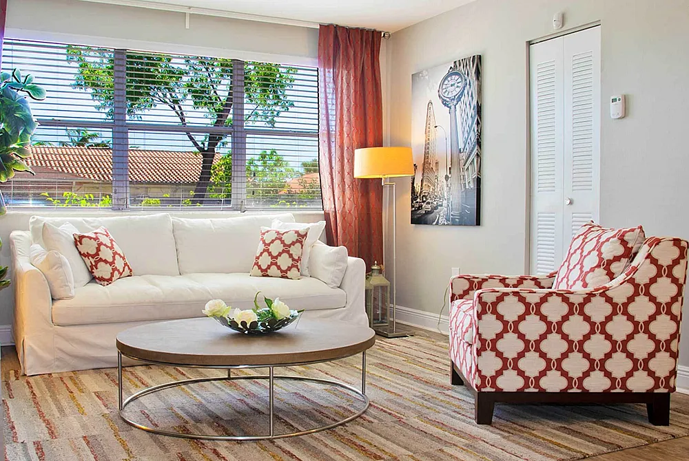 Bright living room with white sofa, patterned armchair, large window, and stylish decor