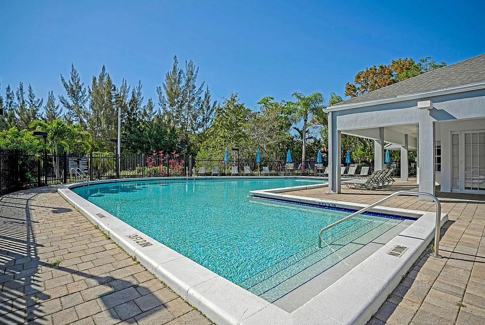 Luxurious outdoor pool area surrounded by lush greenery, featuring comfortable lounge chairs and a shaded patio.