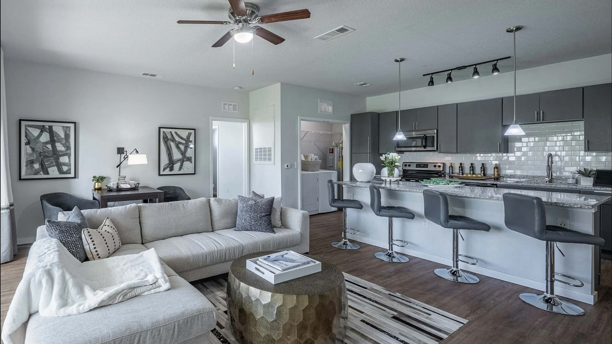 Modern open-concept living space featuring a sleek kitchen with bar seating, stylish gray cabinetry, and a cozy sitting area with chic decor.