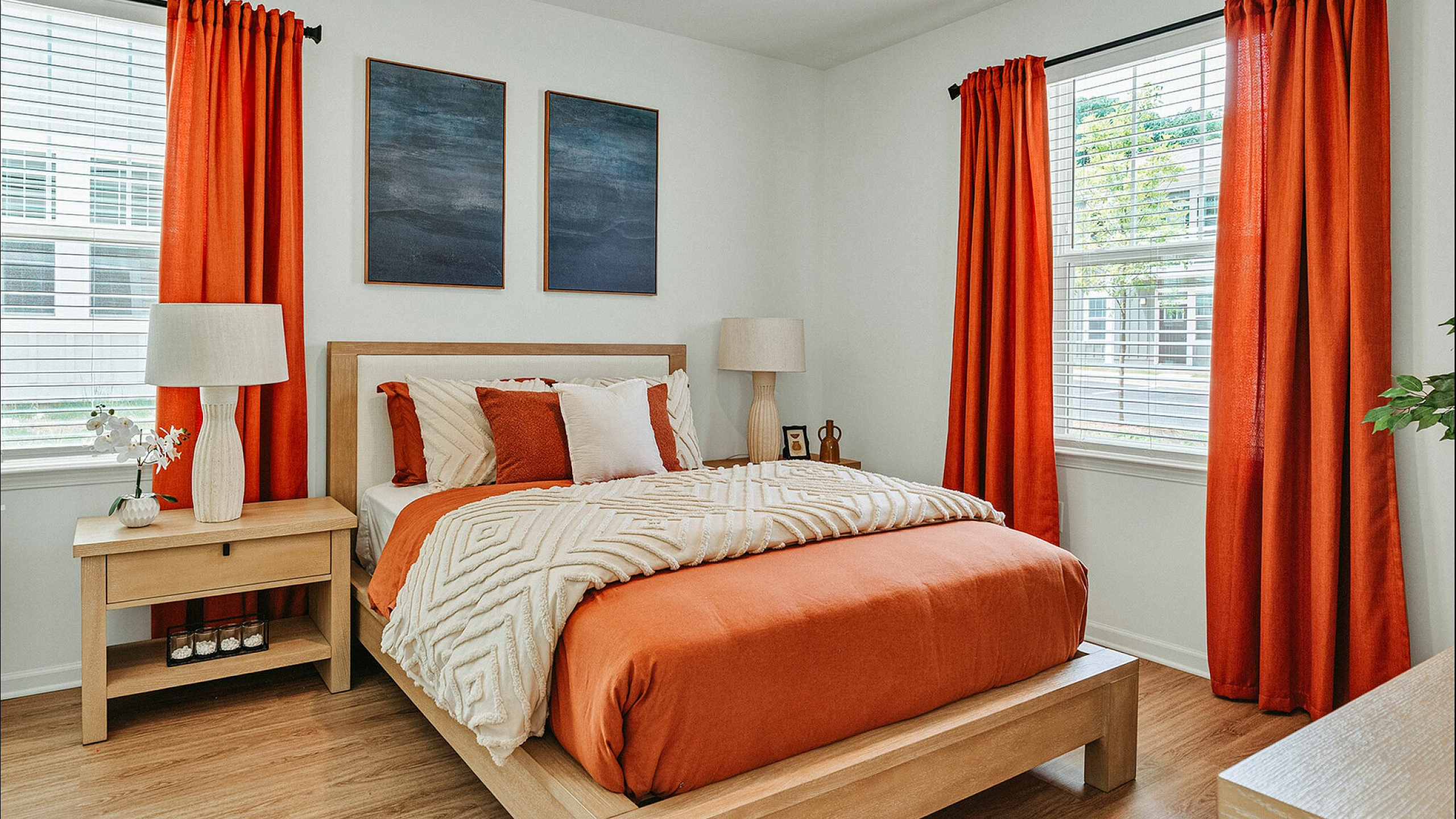 Elegant bedroom featuring warm orange accents, stylish artwork, and abundant natural light.