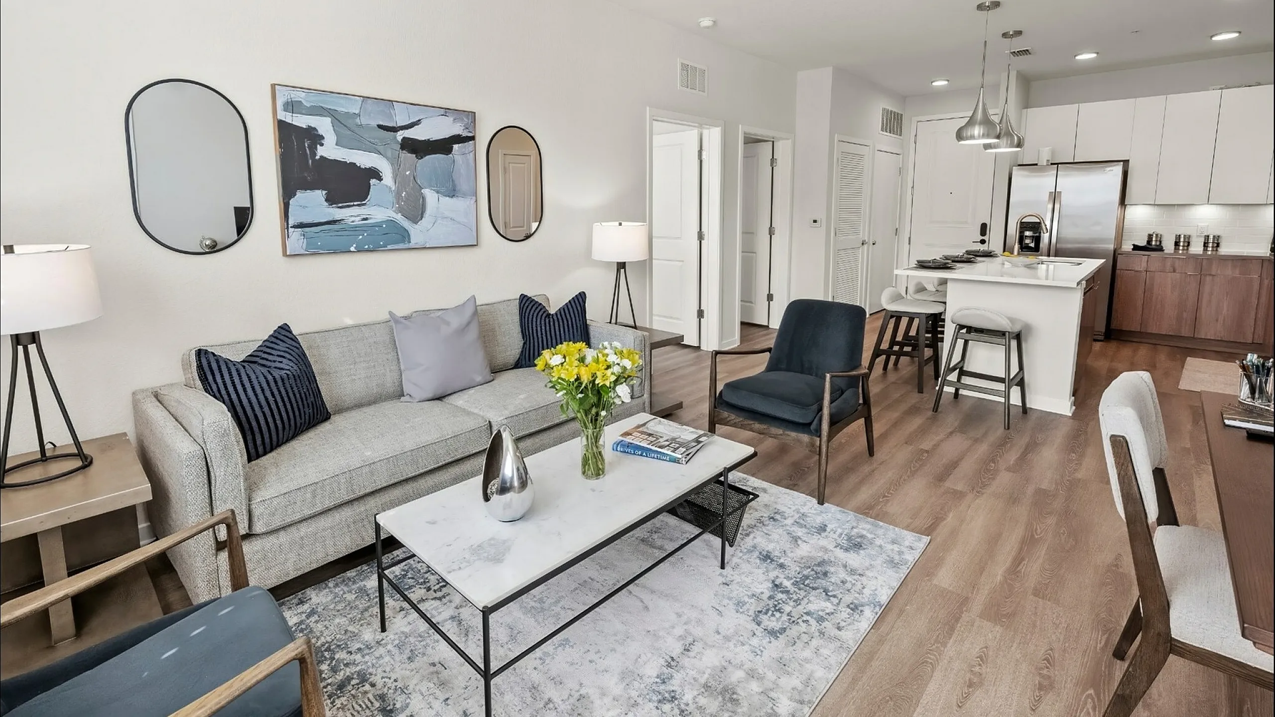 Modern open-plan living area with stylish decor, featuring a cozy seating arrangement, elegant artwork, and a sleek kitchen with stainless steel appliances.