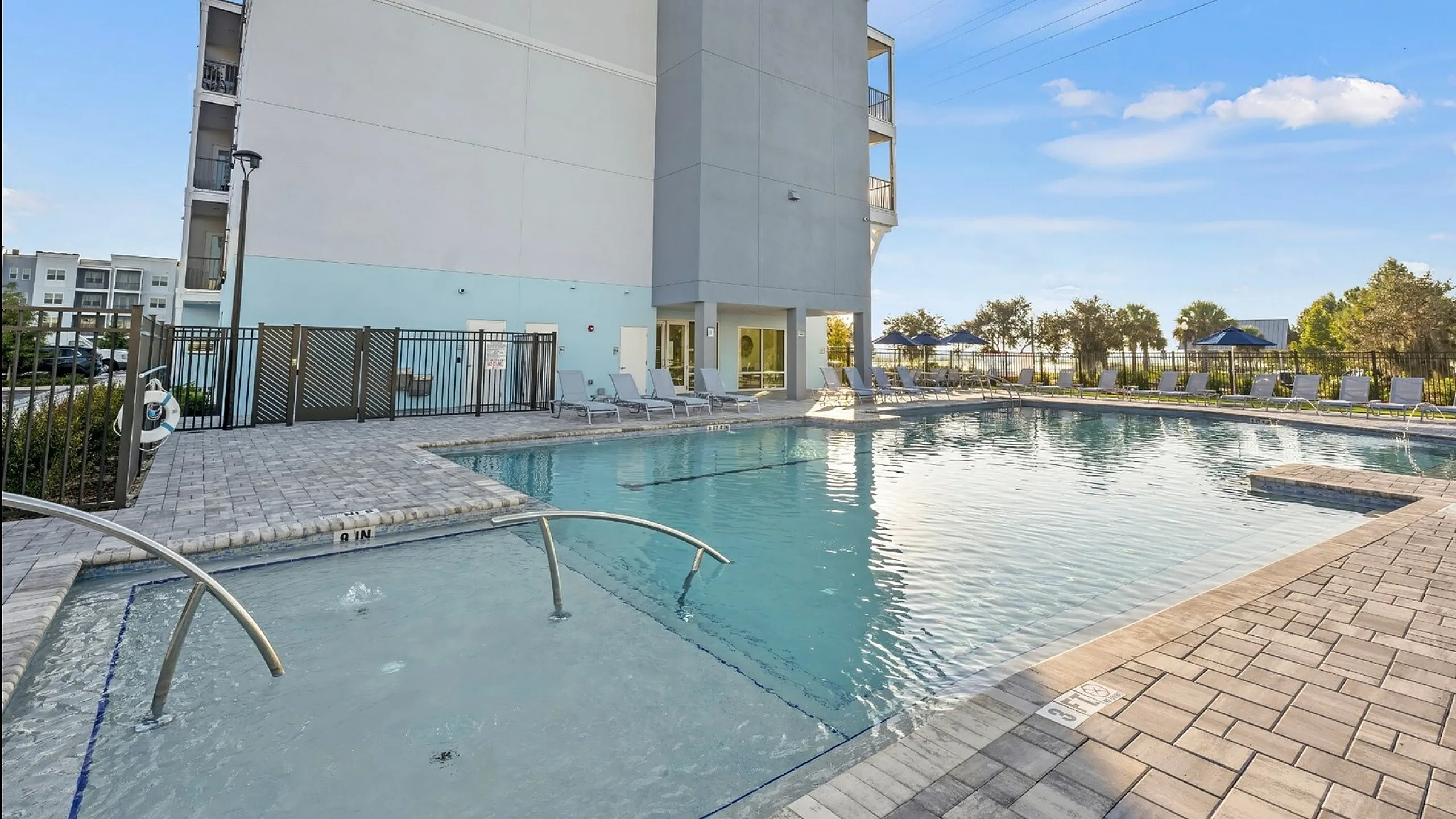 Inviting apartment pool area with sun loungers and modern architecture, set against a bright blue sky.