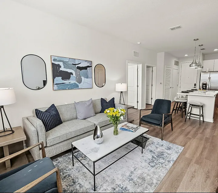 Elegant open-concept living room with modern furniture and a contemporary kitchen, featuring stylish decor and ample natural light.
