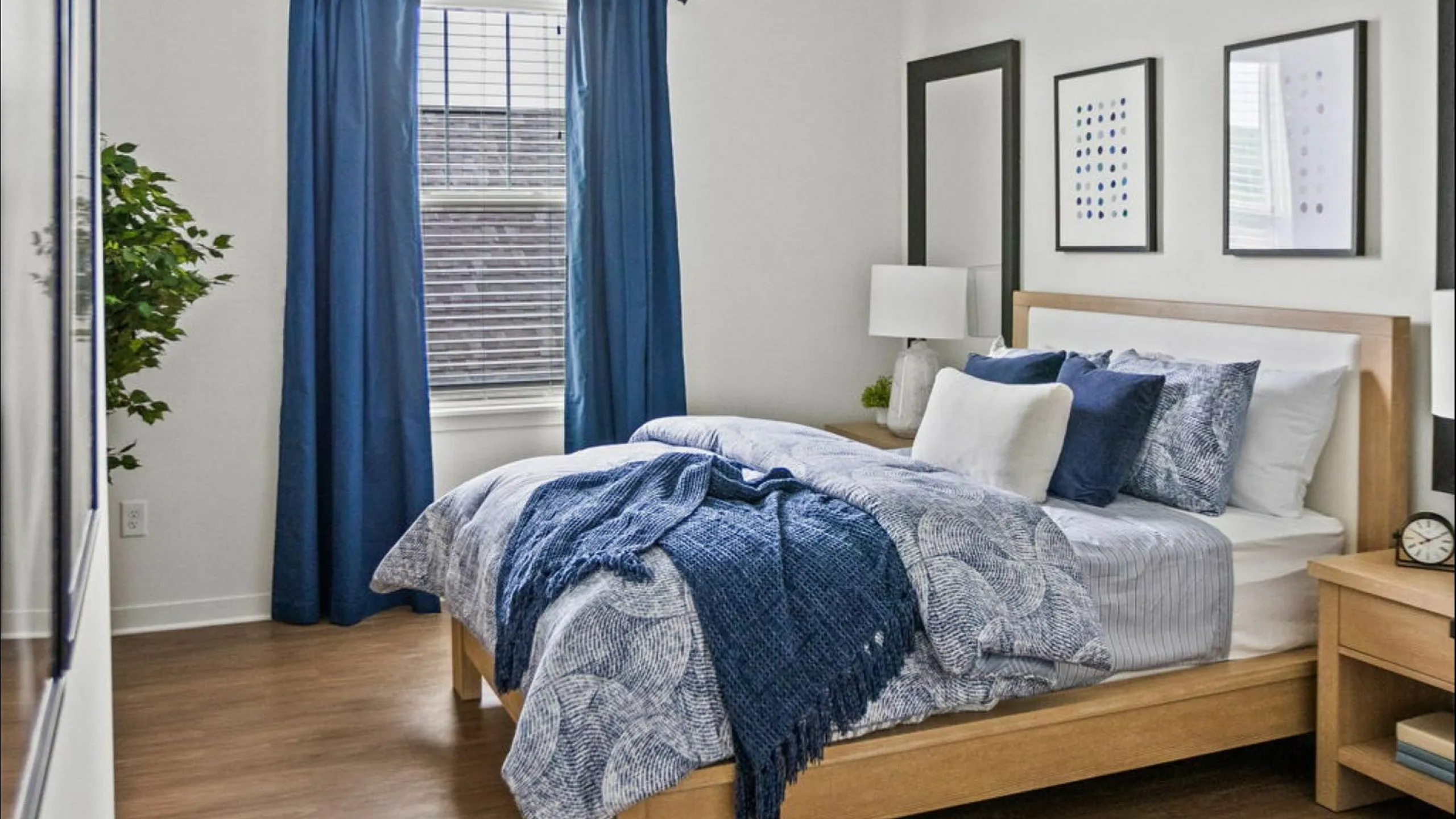 Bright and stylish bedroom with modern decor, featuring a cozy bed dressed in blue and white linens, complemented by natural light and elegant wall art.