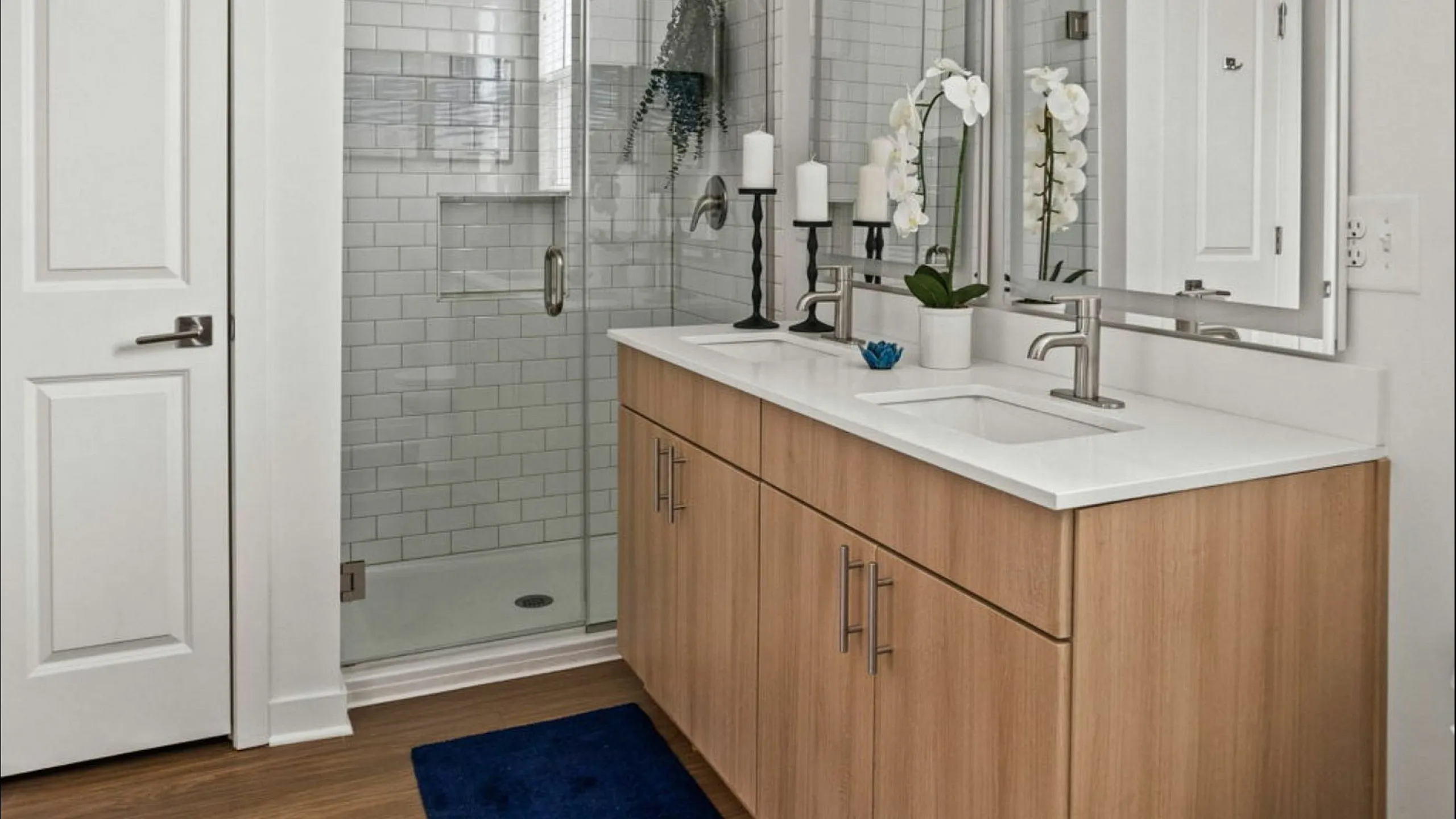 Elegant bathroom featuring a modern glass shower and double sink vanity with chic decor accents.
