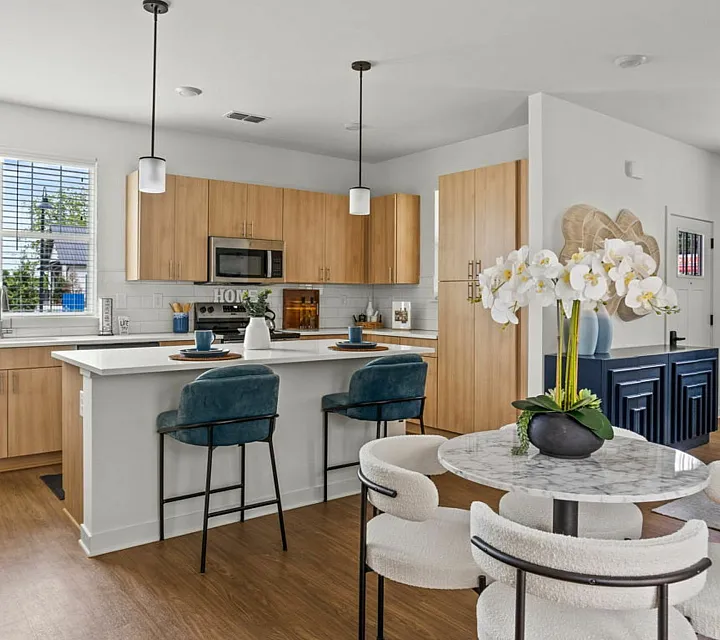 Chic apartment kitchen with modern light wood cabinetry, elegant white countertops, and a stylish dining area featuring plush white chairs and a marble table.
