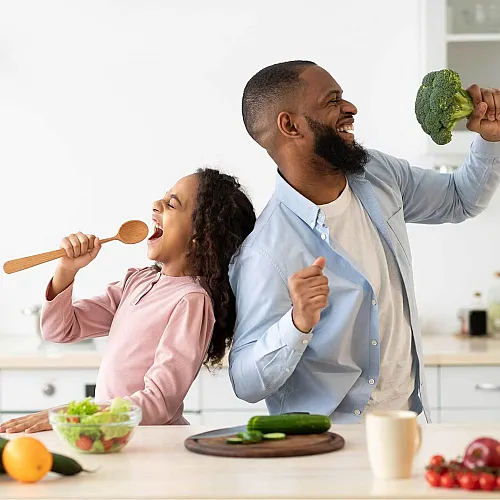 Cheerful father and daughter enjoying a fun moment in a modern kitchen, surrounded by fresh vegetables, embodying healthy living and joy.