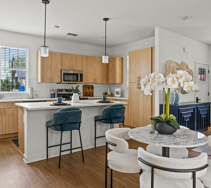 Bright and modern kitchen with sleek wooden cabinets, a chic breakfast bar with stylish blue chairs, and elegant dining area complemented by beautiful orchids.