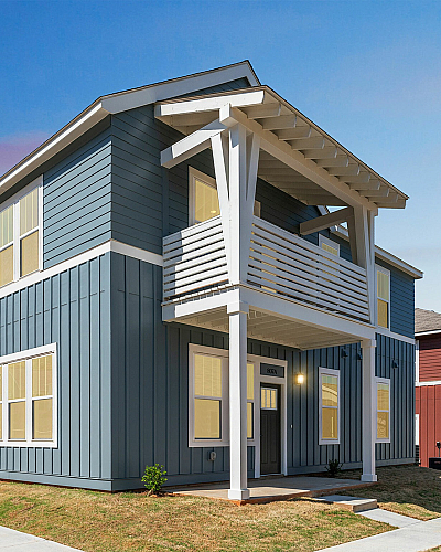 Charming modern two-story blue house with a balcony, large windows, and a welcoming facade in a sunny suburban neighborhood.