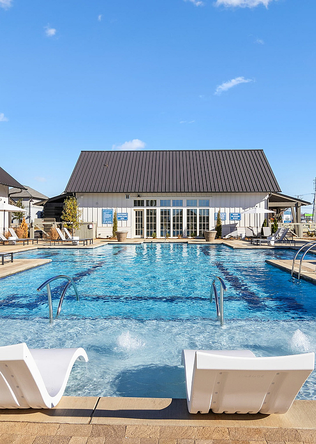Luxurious outdoor swimming pool area with elegant lounge chairs and modern clubhouse under a clear blue sky.