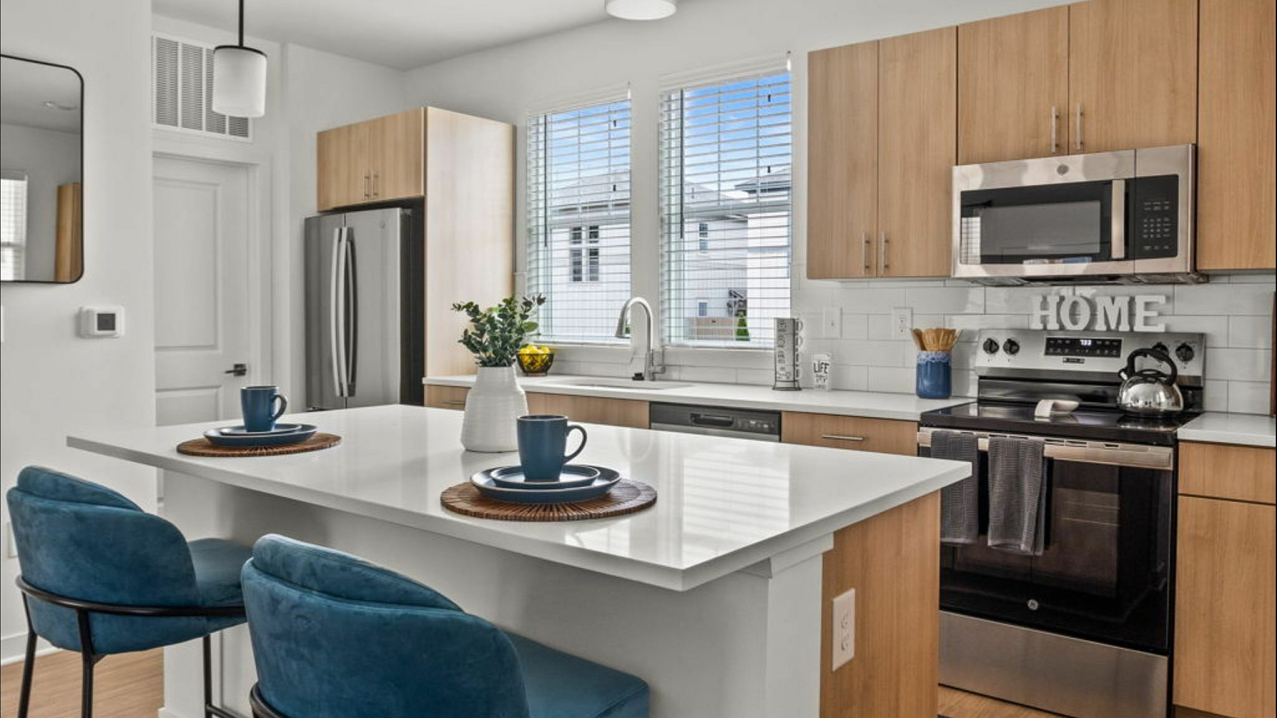 Bright and modern kitchen with sleek stainless steel appliances, stylish wood cabinets, and a cozy breakfast bar adorned with elegant blue chairs.