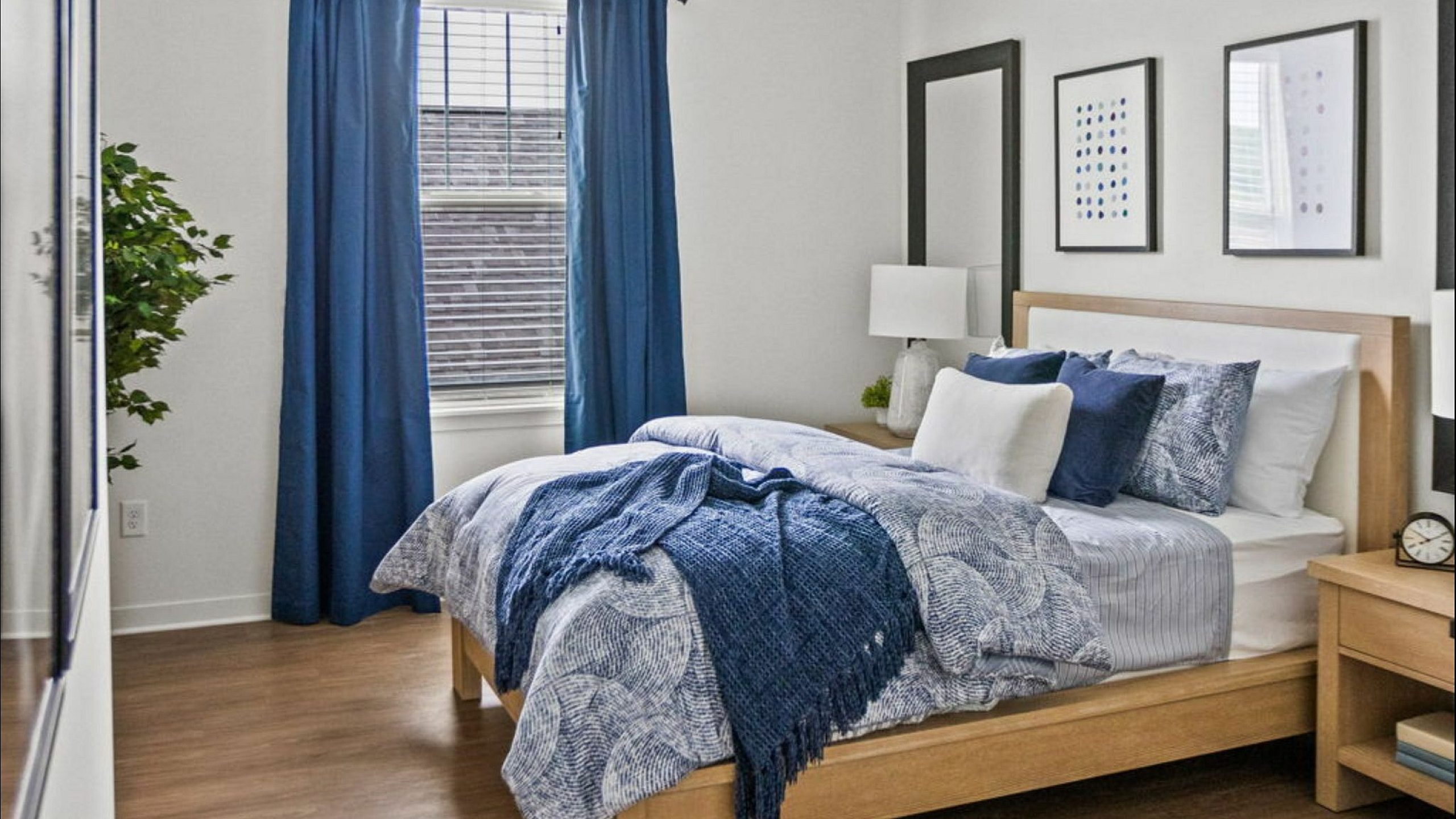 Inviting bedroom with elegant blue accents, stylish wooden furniture, and natural light through a large window.