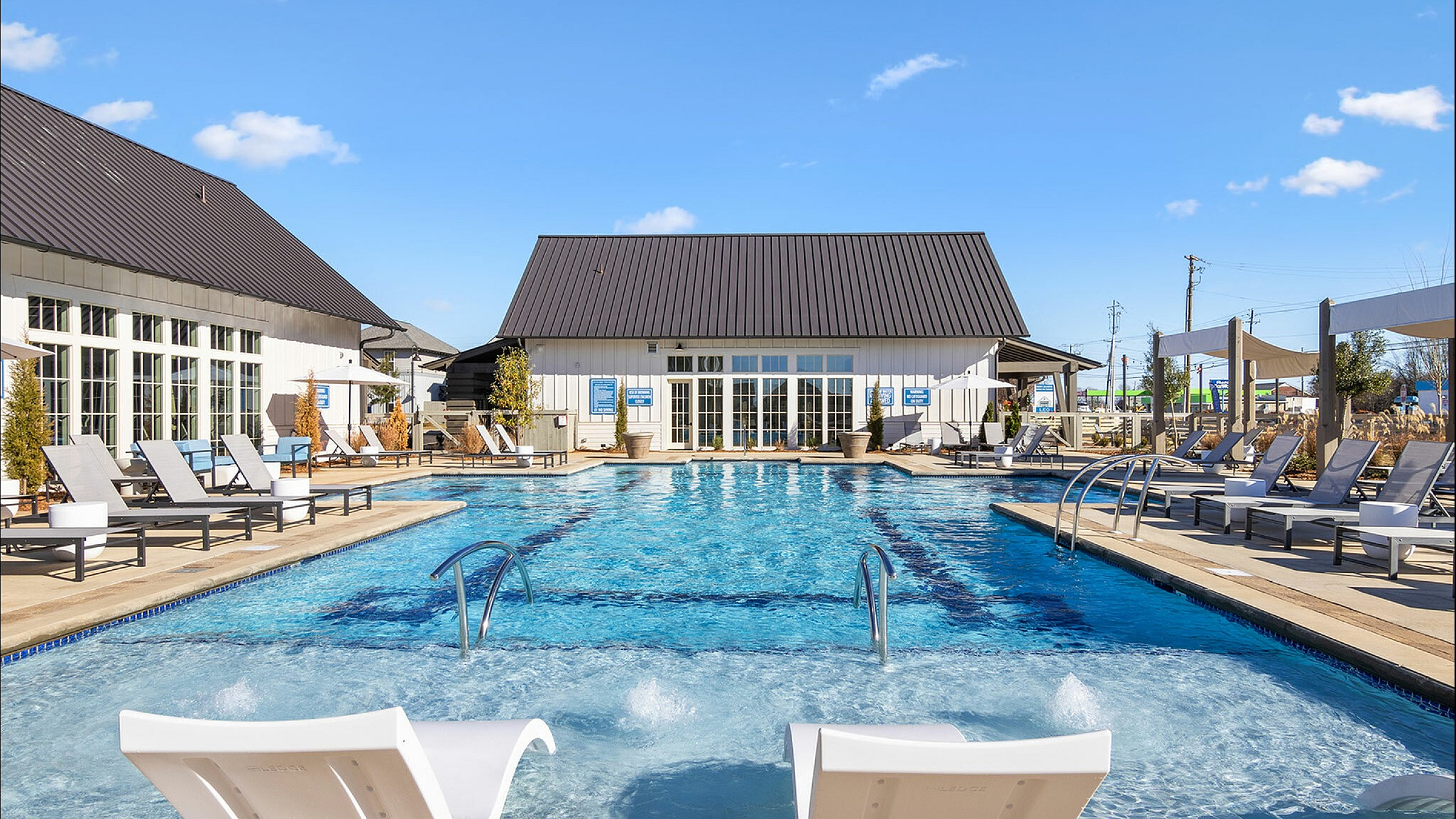 Luxurious outdoor pool area with elegant lounge chairs, surrounded by modern architecture and vibrant greenery under a clear blue sky.