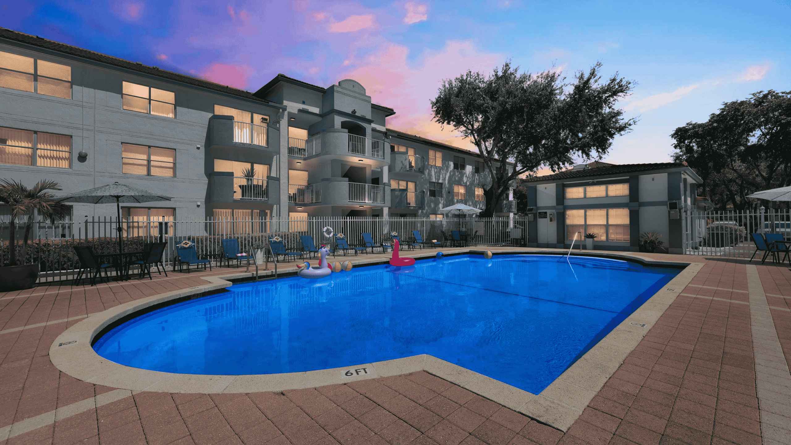 Charming apartment complex with a vibrant swimming pool, surrounded by inviting lounge chairs and a tranquil sunset sky.