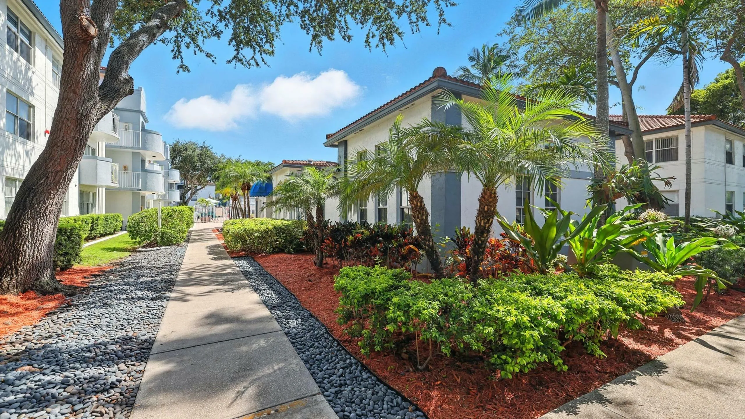 Vibrant tropical landscaping surrounds a charming apartment building, creating a serene and inviting pathway.