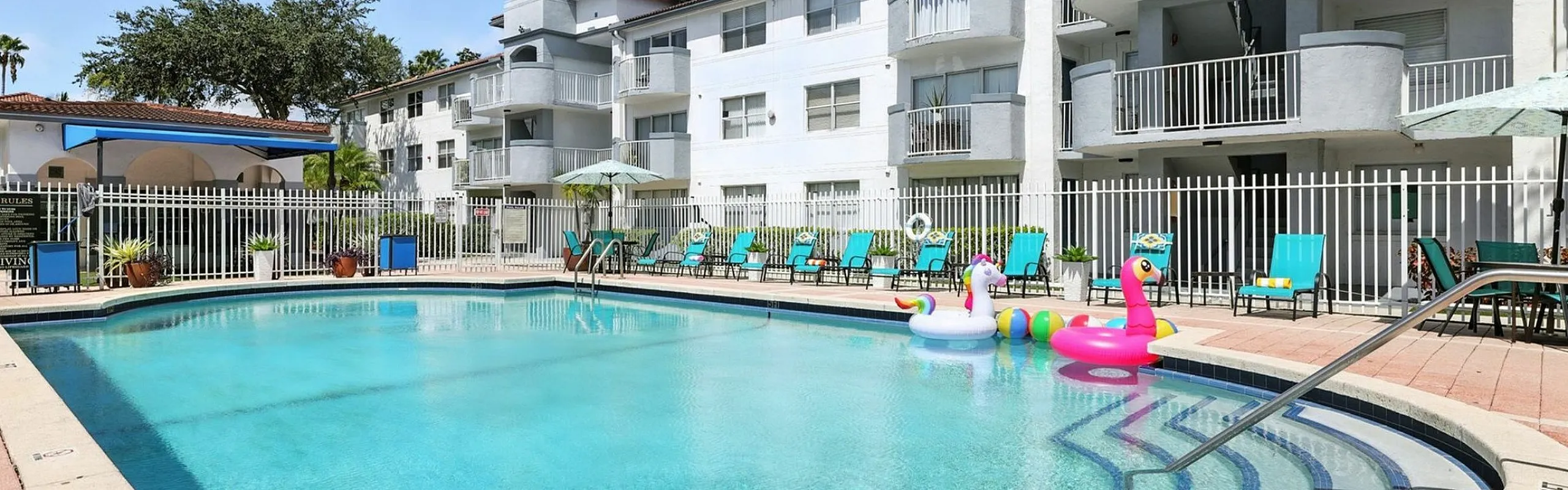 Inviting apartment complex with a sparkling swimming pool, surrounded by lounge chairs and playful inflatables, perfect for relaxation and leisure.