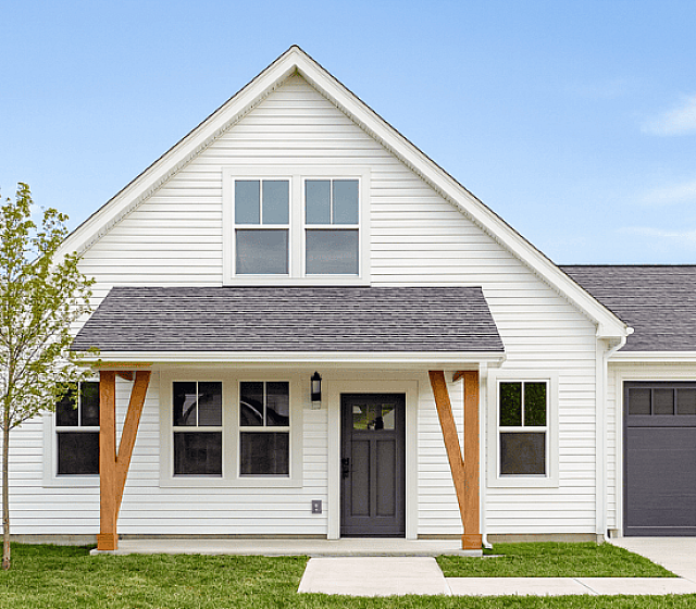 Charming single-story white home with a gabled roof, inviting front porch, and lush green lawn.