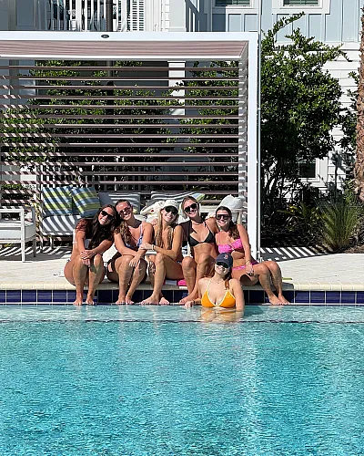 Vibrant poolside scene with a group enjoying sunshine in a luxurious apartment complex setting, featuring modern outdoor lounge spaces and lush greenery.