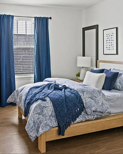 Inviting bedroom with elegant blue accents, cozy bed, and natural light streaming through large window.