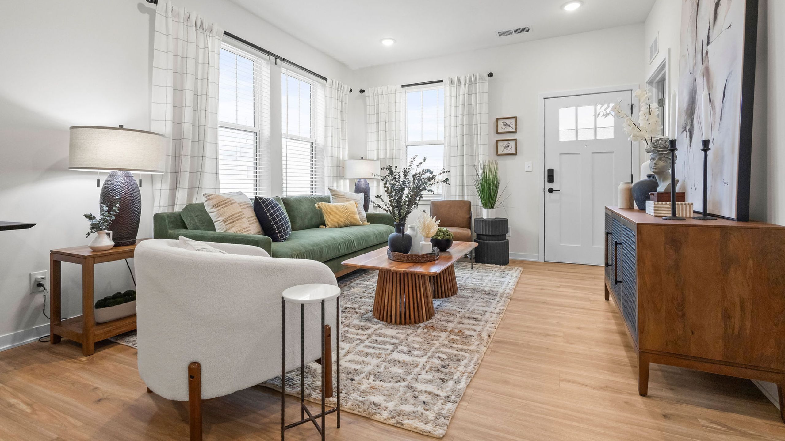 Chic and inviting living room with modern d&eacute;cor, featuring a plush green sofa, elegant wooden coffee table, and ample natural light for a cozy atmosphere.