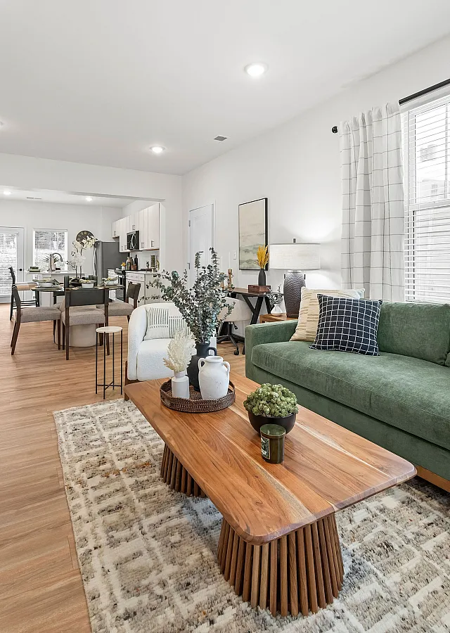 Chic open-concept living space featuring a stylish wooden coffee table, plush green sofa, and modern dining area with inviting natural light.
