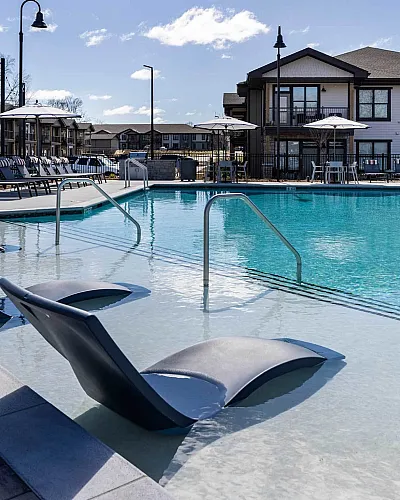 Luxurious apartment complex pool area with modern lounge chairs, inviting crystal-clear water, and elegant architecture in the background.