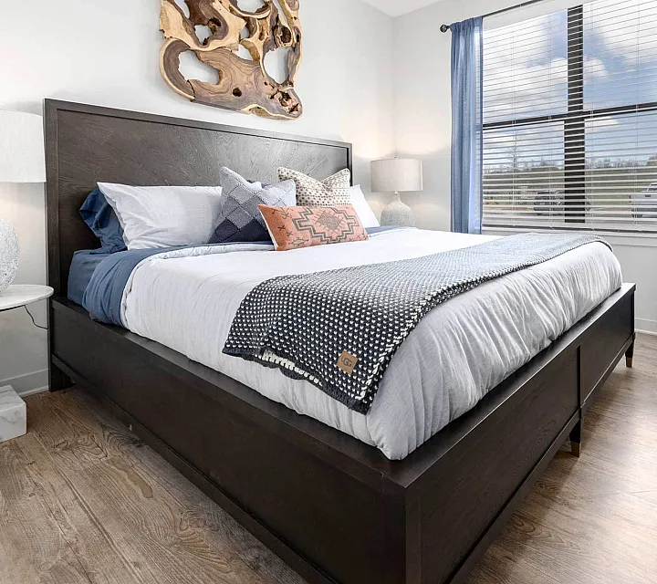Elegant bedroom with a luxurious king-sized bed, stylish decor, and a large window with blue curtains, offering a bright and inviting atmosphere.