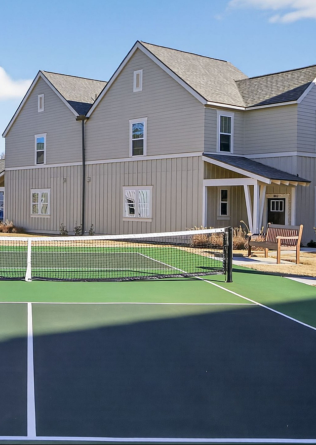 Inviting residential neighborhood with modern houses flanking a well-maintained tennis court, offering a blend of community and recreation.