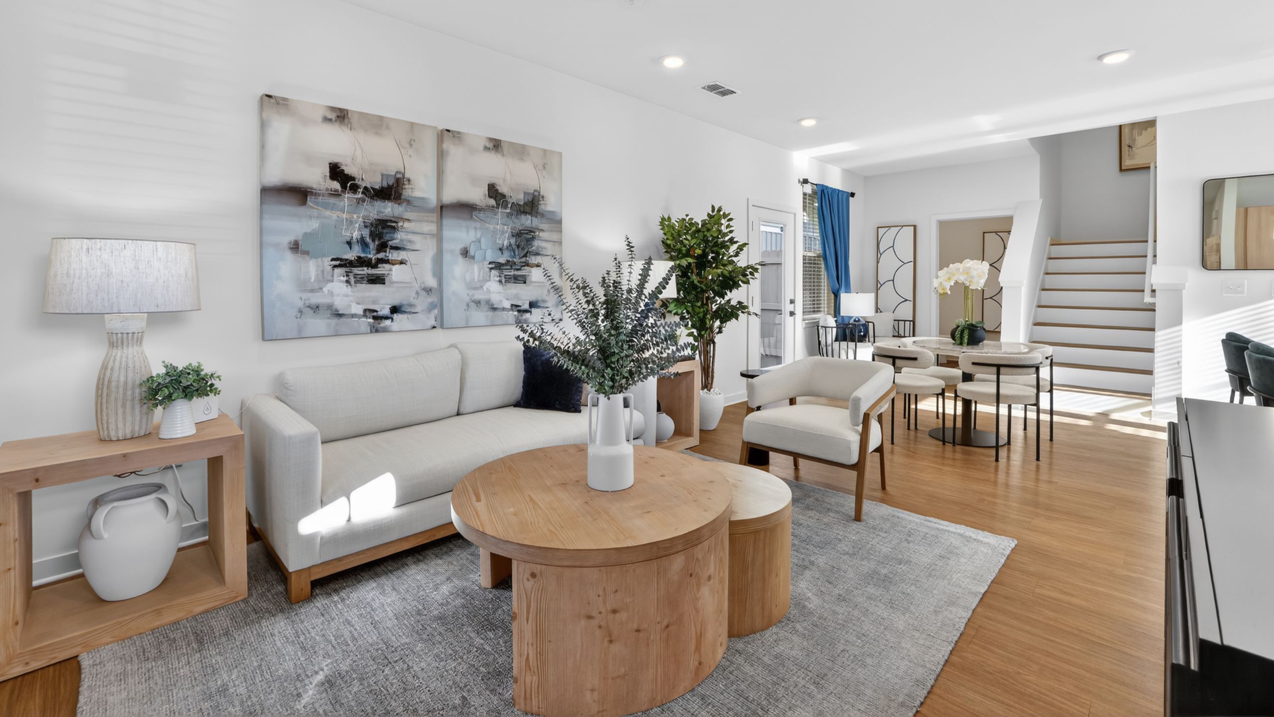 Elegant, modern living room with chic decor, featuring a cozy sofa, stylish coffee table, and bright natural lighting; open to dining area with tasteful furnishings.
