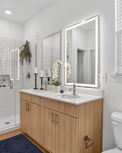 Modern bathroom featuring a sleek double sink vanity with wooden cabinets, illuminated mirrors, a spacious glass-door shower, and elegant decor accents.
