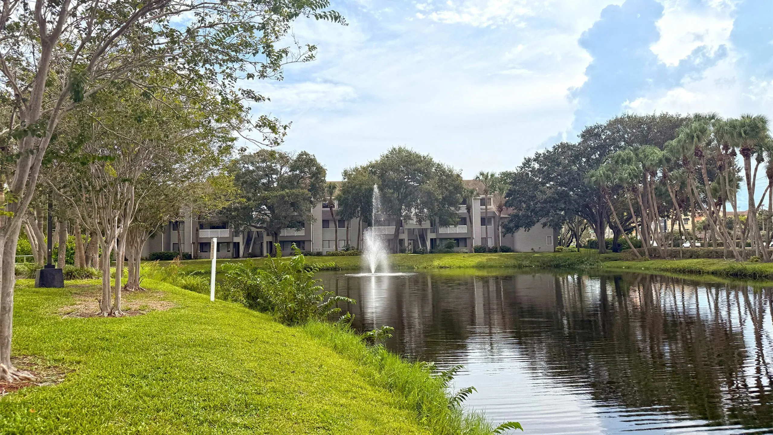 Serene lakeside apartment community surrounded by lush greenery and a tranquil fountain, perfect for nature lovers.