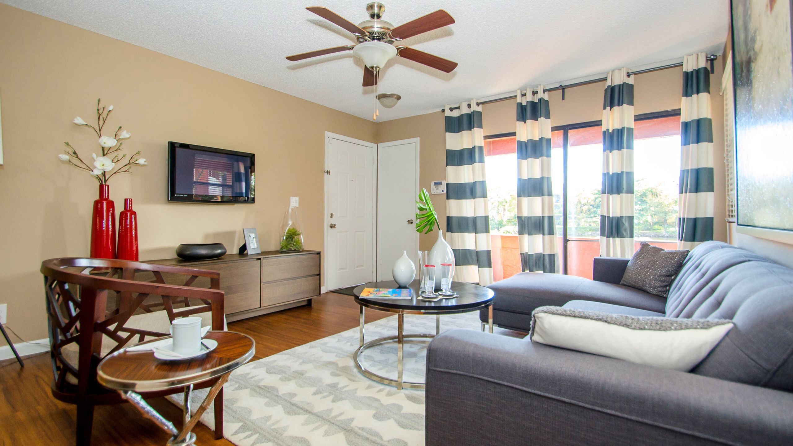 Bright and inviting living room with modern decor, featuring a comfortable gray sofa, stylish wooden chair, and elegant furnishings, all set against a backdrop of patterned drapes and warm tones.