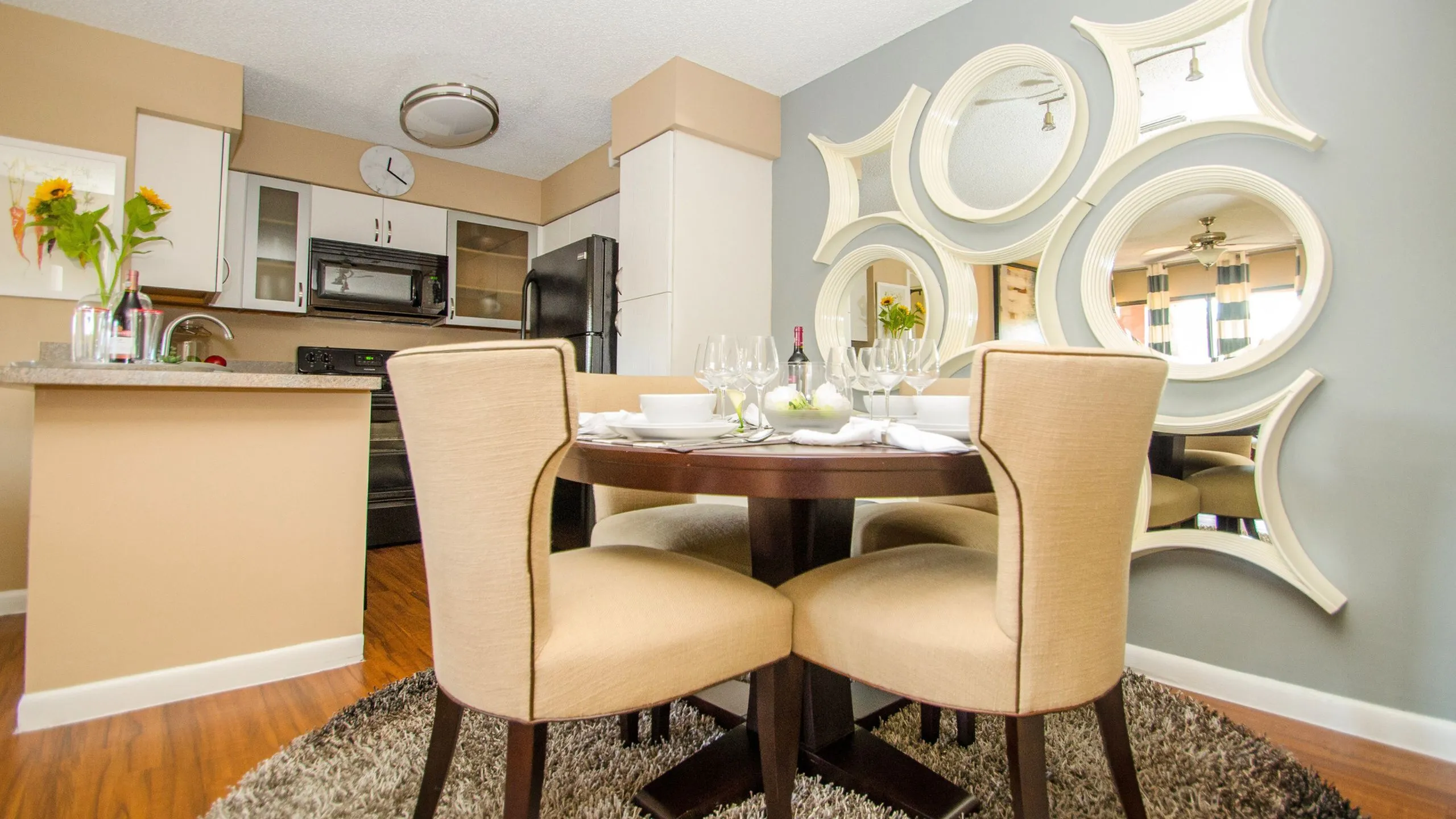 Inviting dining area with elegant round table and plush chairs, set against a modern kitchen backdrop featuring chic mirrors and vibrant decor.